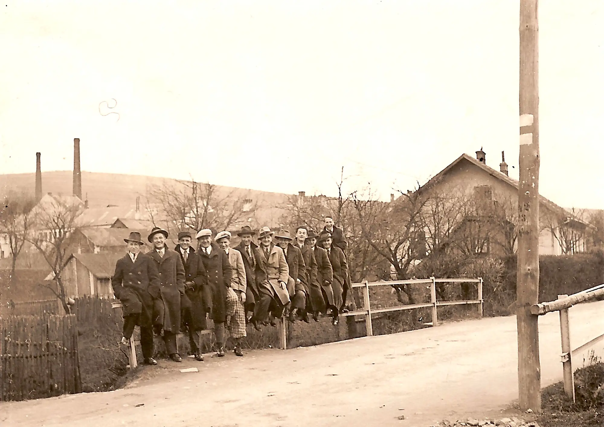 Zwart-witfoto uit de jaren dertig van glasarbeiders bij de fabriek, met de schoorstenen op de achtergrond